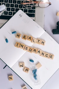 close up top view of desk with laptop and notebook with health insurance spelled out with scrabble letters