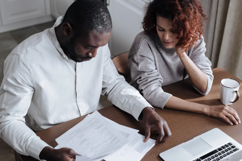 couple reviewing paperwork together at home dining table with laptop