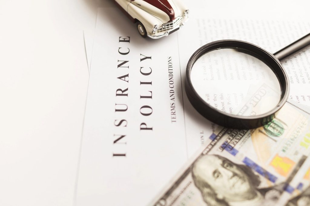 Insurance policy documents, a magnifying glass and cash representing the cost of insurance coverage