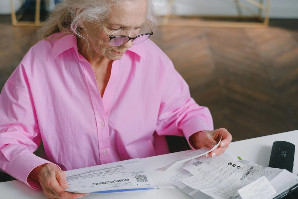 Senior woman reviewing bills and paperwork to understand healthcare expenses and insurance costs